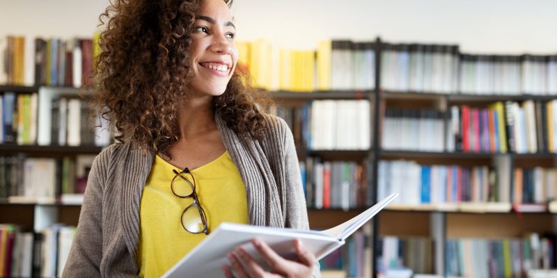 Education, high school, university, learning and people concept. Smiling happy student girl reading book at library